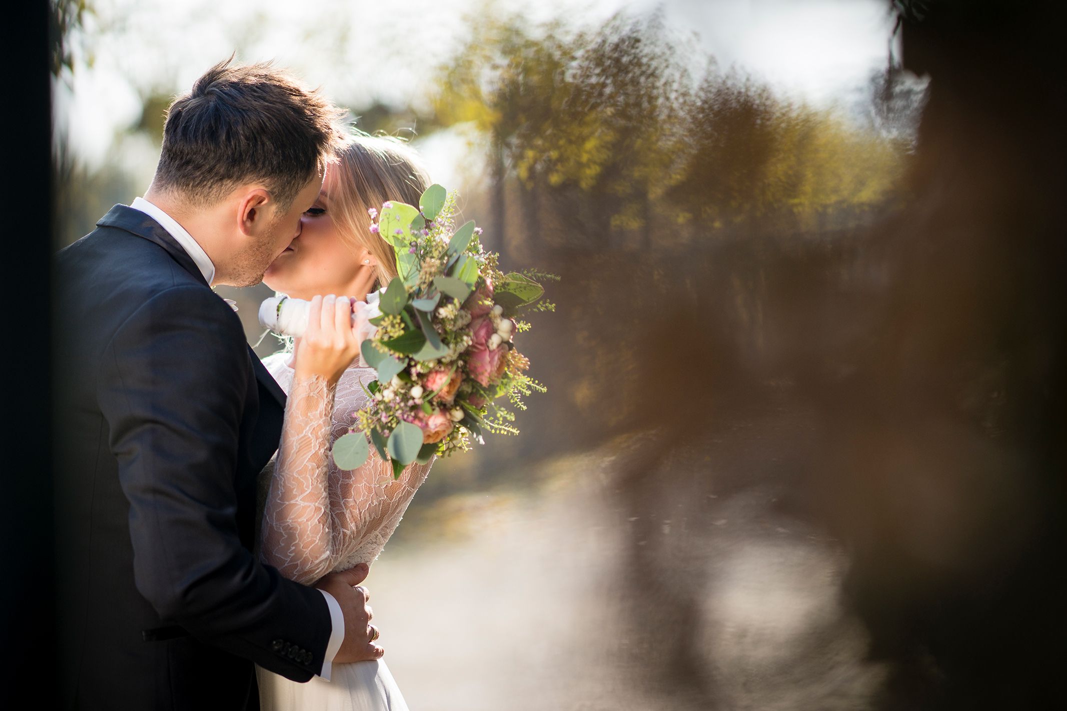 Brautpaar küsst sich im Gegenlicht der Sonne am Waldrand
