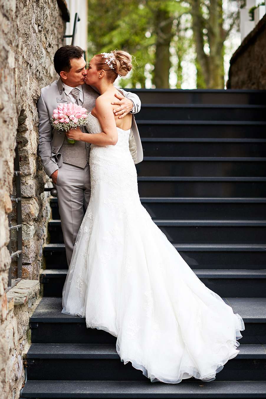 Brautpaar küsst sich auf einer Treppe, emotionales Paarfoto im Freien.